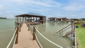 Un muelle de madera que conduce a un embarcadero con una zona de estar cubierta y un pequeño edificio.