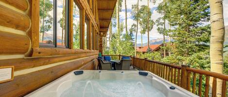 A wooden cabin with a hot tub on a deck, overlooking a mountainous landscape.
