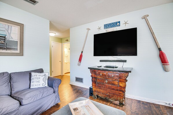 A living room with a grey sofa, a wooden chest of drawers, a television, and two hammers on the wall. - Cape Canaveral Cottage w/ Hot Tub: Walk to Beach (Cape Canaveral)