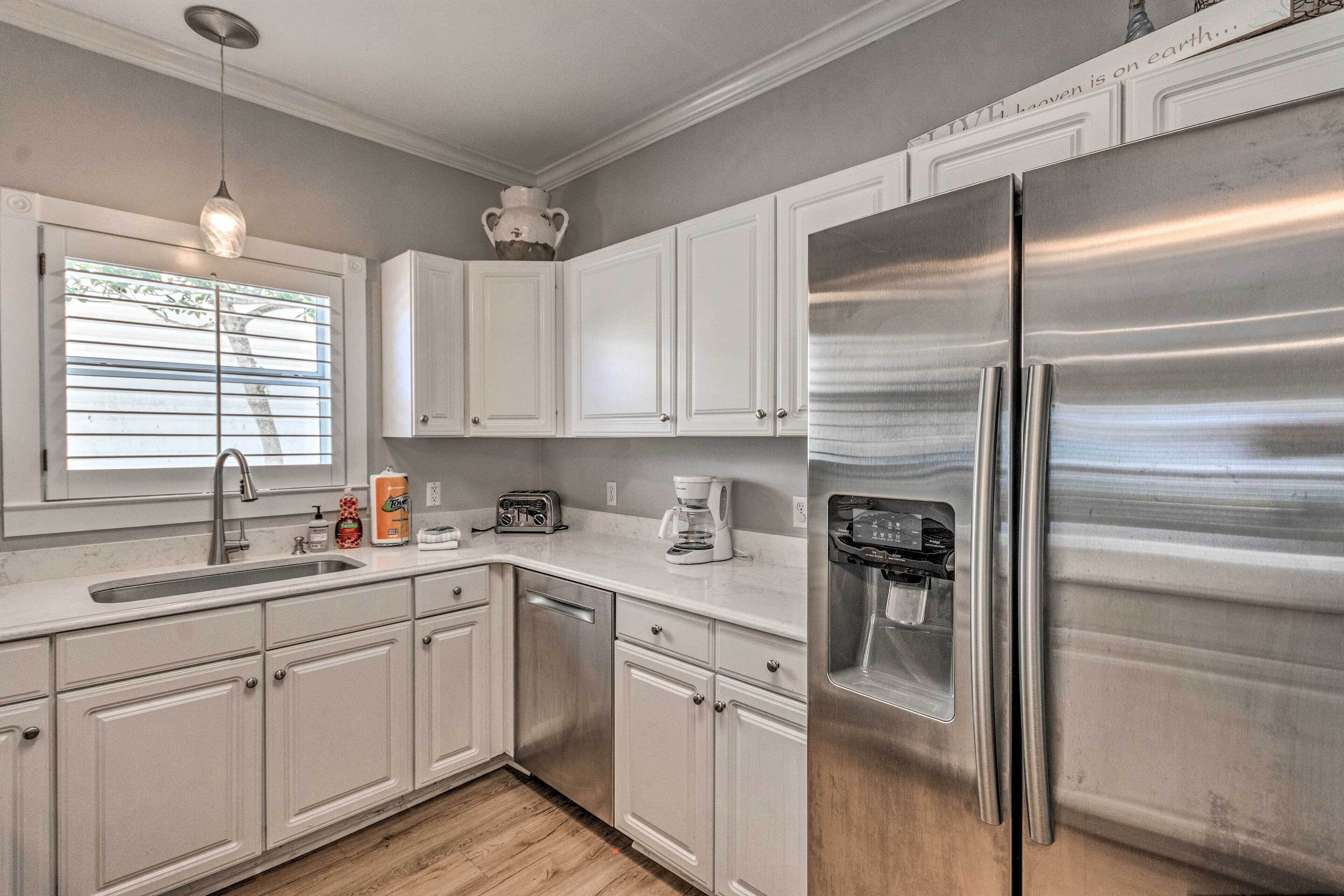 A modern kitchen with white cabinets, stainless steel appliances, and a window with blinds.