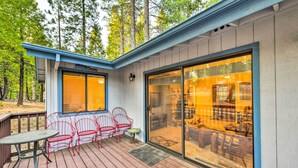 A covered deck with a table and red chairs, a sliding glass door leading to an interior space, and a wooden deck.