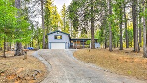 A cabin with a garage, surrounded by tall trees and a dirt path leading to it.