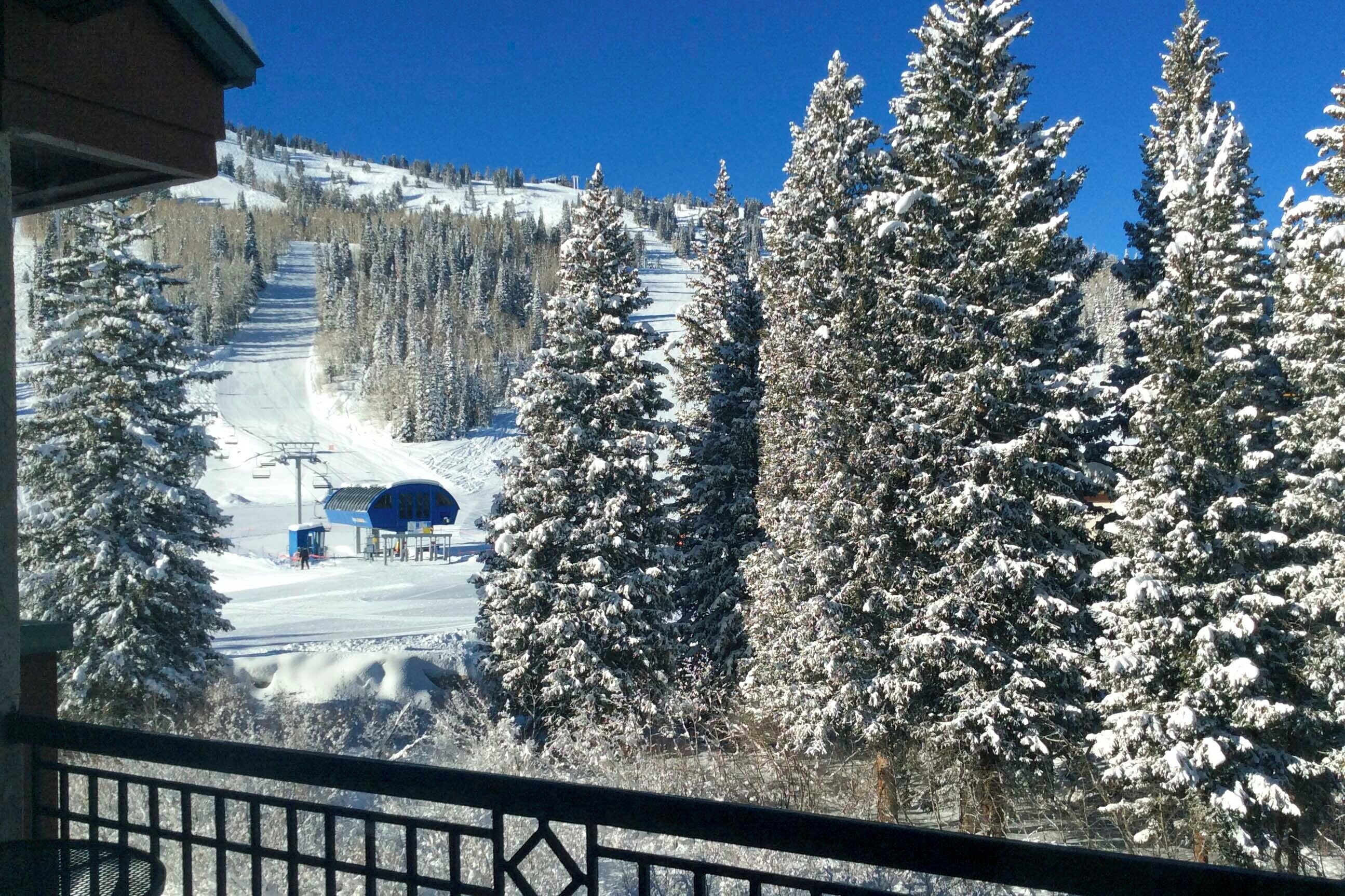 A snow-covered ski slope with a ski lift and a blue building in the distance.