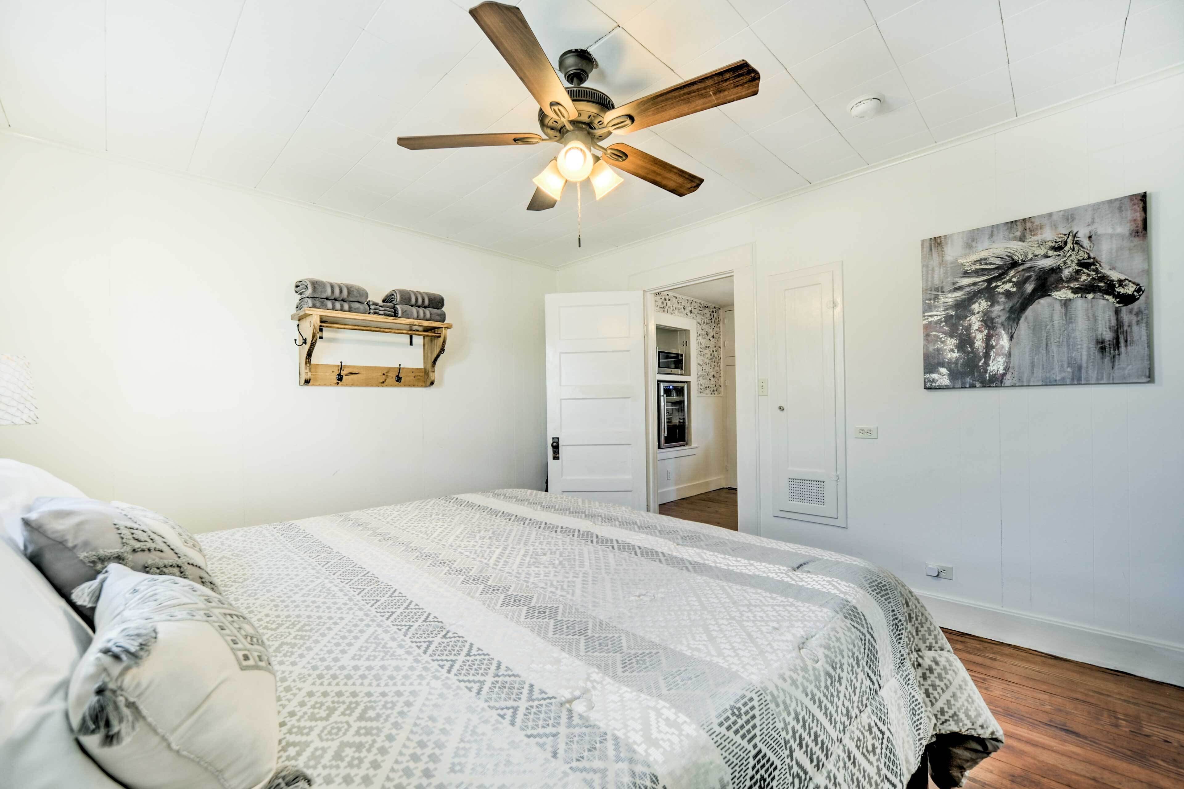 A bedroom with a bed, a ceiling fan, a door leading to a bathroom, and a wall-mounted shelf.