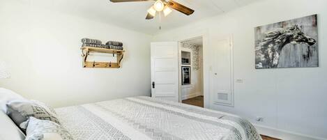 A bedroom with a bed, a ceiling fan, a door leading to a bathroom, and a wall-mounted shelf.