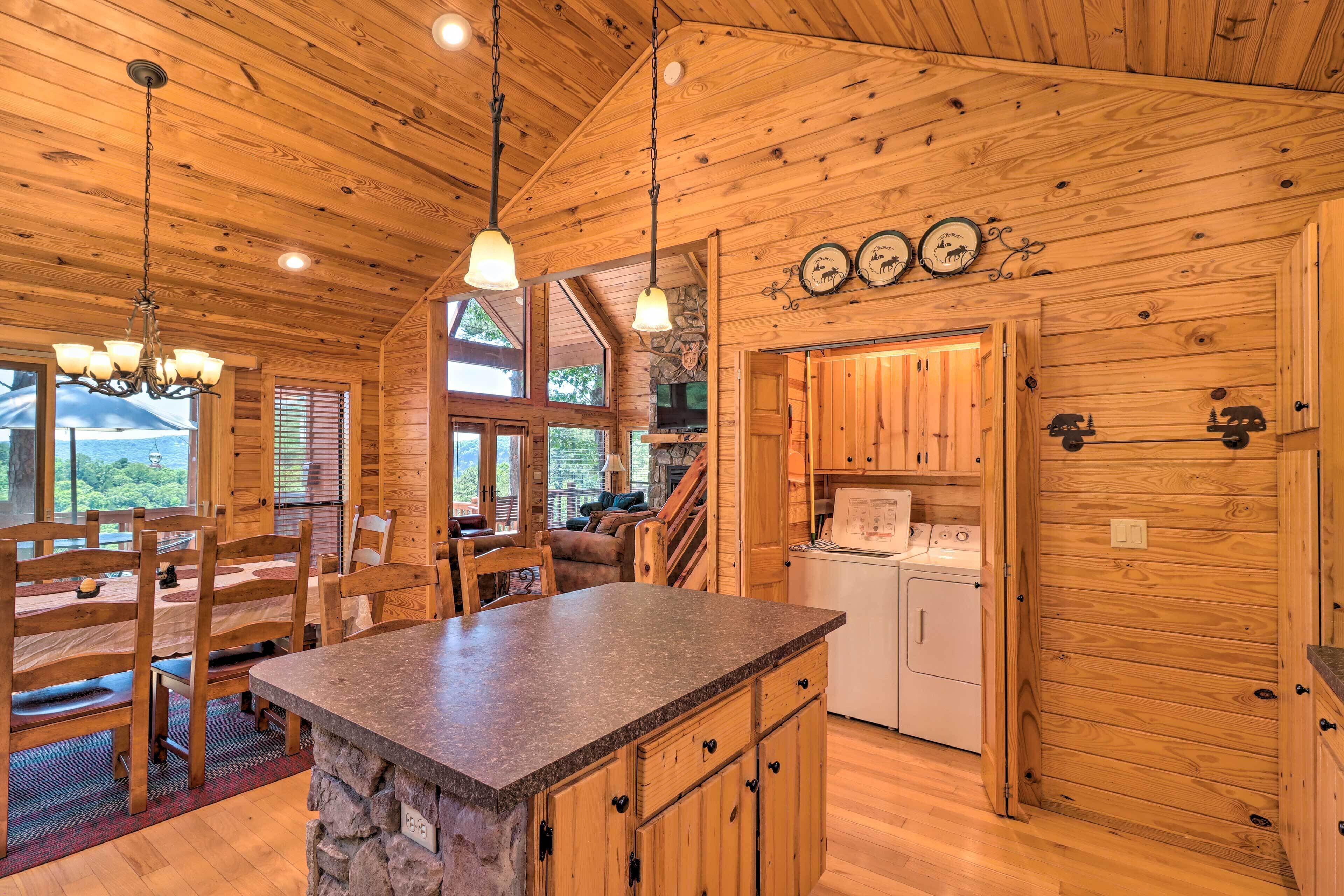 A wooden cabin interior with a kitchen, dining area, and a stone fireplace.