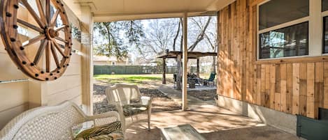 A covered patio area with wicker furniture, a wooden wheel, and a view of the backyard.