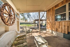 Un patio couvert, aménagé avec des meubles en osier, une roue en bois et offrant une vue sur le jardin arrière.