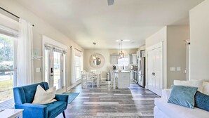 A spacious living area with a blue sofa and white couch, a kitchen in the background, and large windows allowing natural light. - Modern Santa Rosa Beach Retreat w/ Yard & Patio! (Santa Rosa Beach)