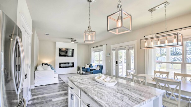 A modern kitchen with a marble island, pendant lights, and a dining area with white furniture. - Modern Santa Rosa Beach Retreat w/ Yard & Patio! (Santa Rosa Beach)