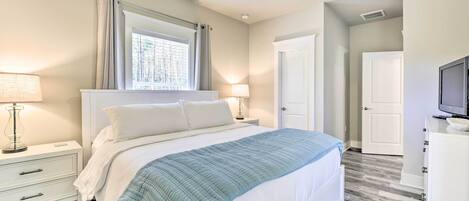 A bedroom with a bed, two bedside tables with lamps, a ceiling fan, a window with curtains, and a door.