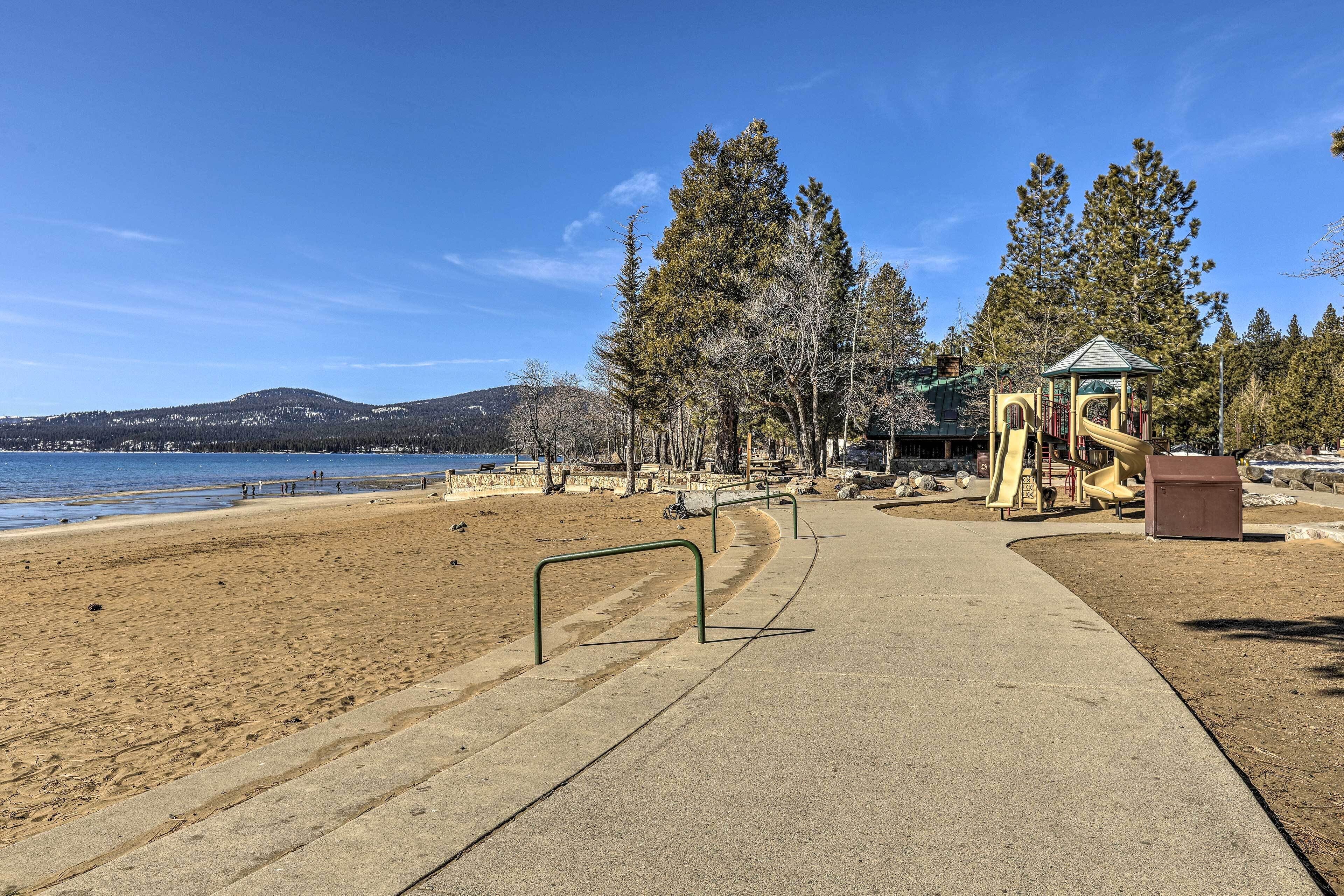 A beach with a concrete path, playground, and a small gazebo.