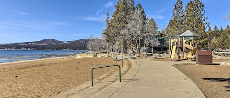 A beach with a concrete path, playground, and a small gazebo.