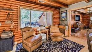 A log cabin interior with leather chairs, a rug, a wooden table, and a large window.