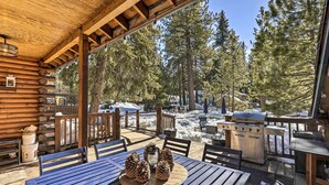 A wooden deck with outdoor seating, a grill, and a view of a snowy forest.