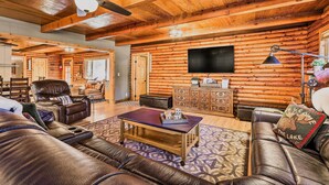A spacious living room with leather sofas, a coffee table, and a ceiling fan.