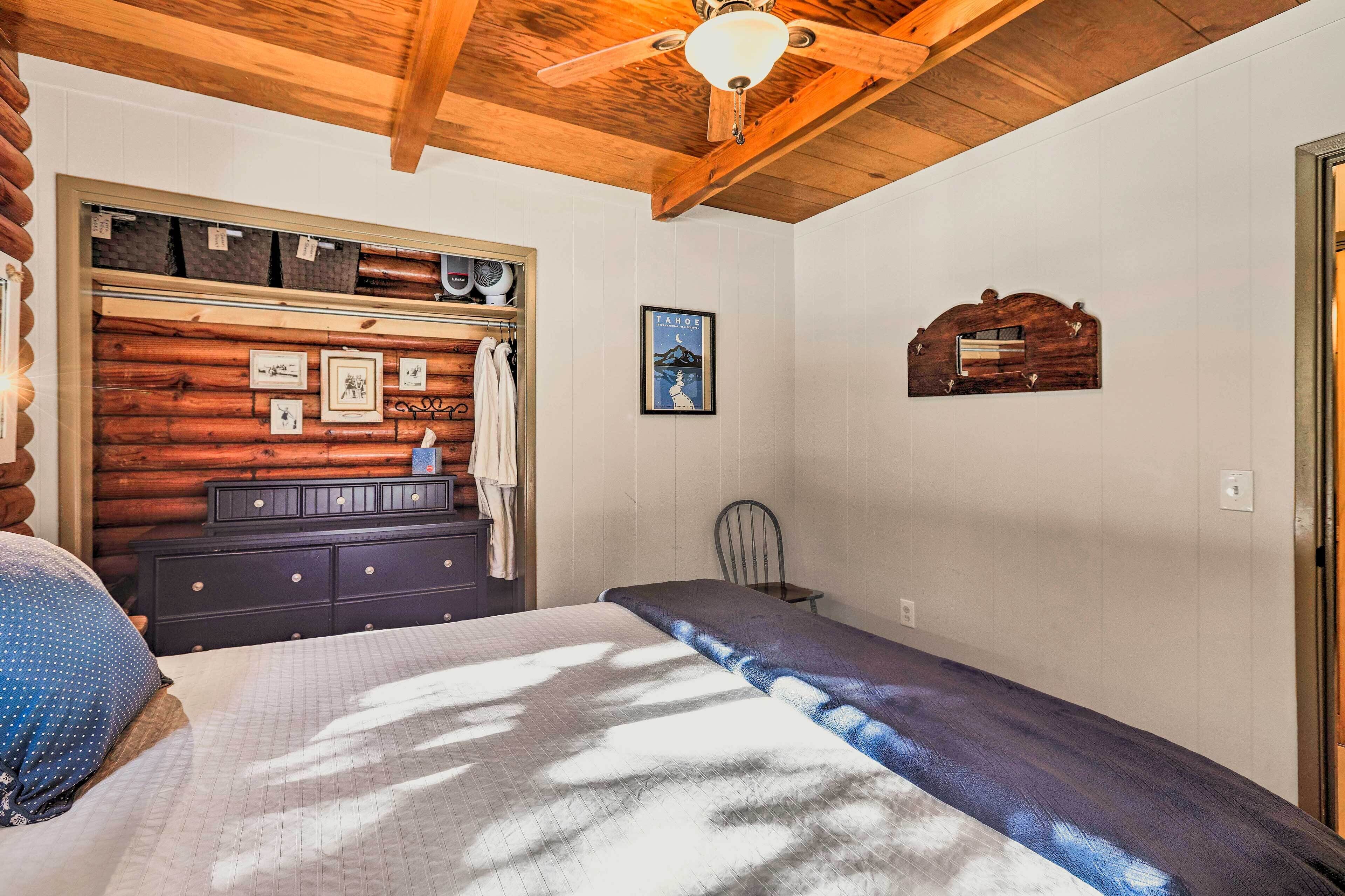 Un dormitorio con cabecera de madera, cama con colcha de diseño azul y blanco, cómoda de madera y ventilador de techo.