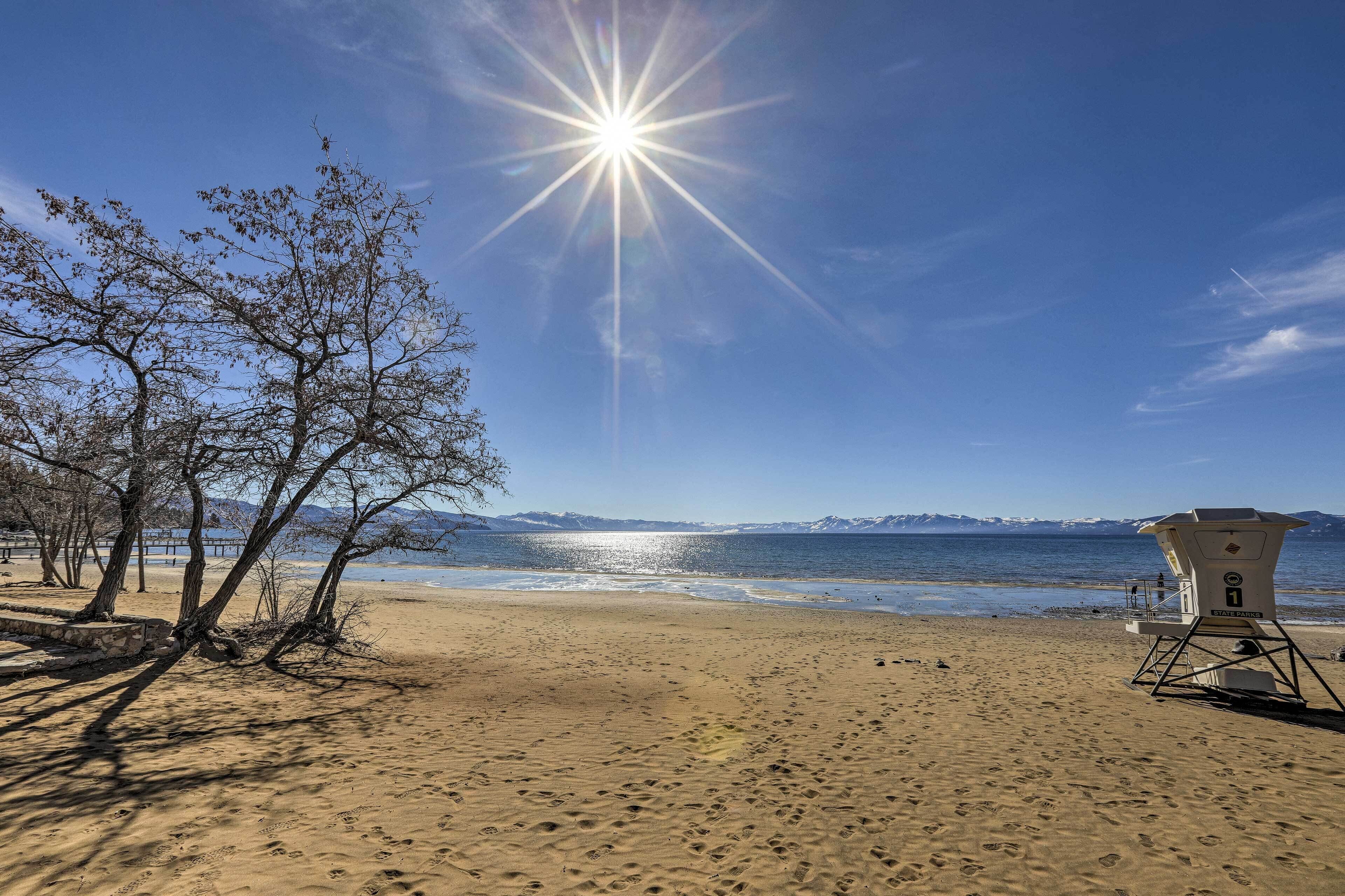A beach with footprints, a lifeguard tower, and mountains in the background.