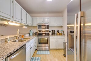 A modern kitchen with white cabinets, stainless steel appliances, granite countertops, and a blue checkered rug.