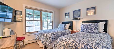 A bedroom with two beds, a desk, and a window.