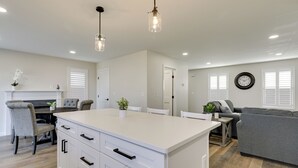 A modern kitchen with white cabinetry, a central island, pendant lighting, and a dining area with chairs and a table. - Renovated Family Home on Providence River! (Riverside)