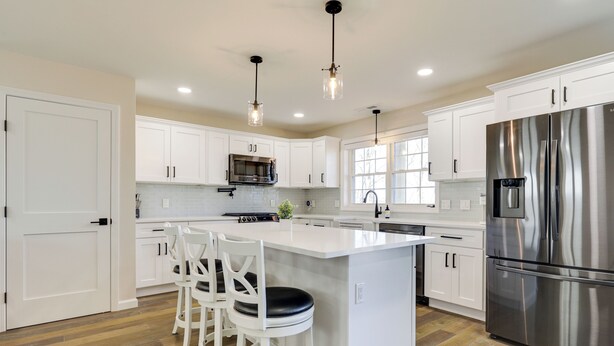 A modern kitchen with white cabinetry, a stainless steel refrigerator, and a central island with bar stools. - Renovated Family Home on Providence River! (Riverside)