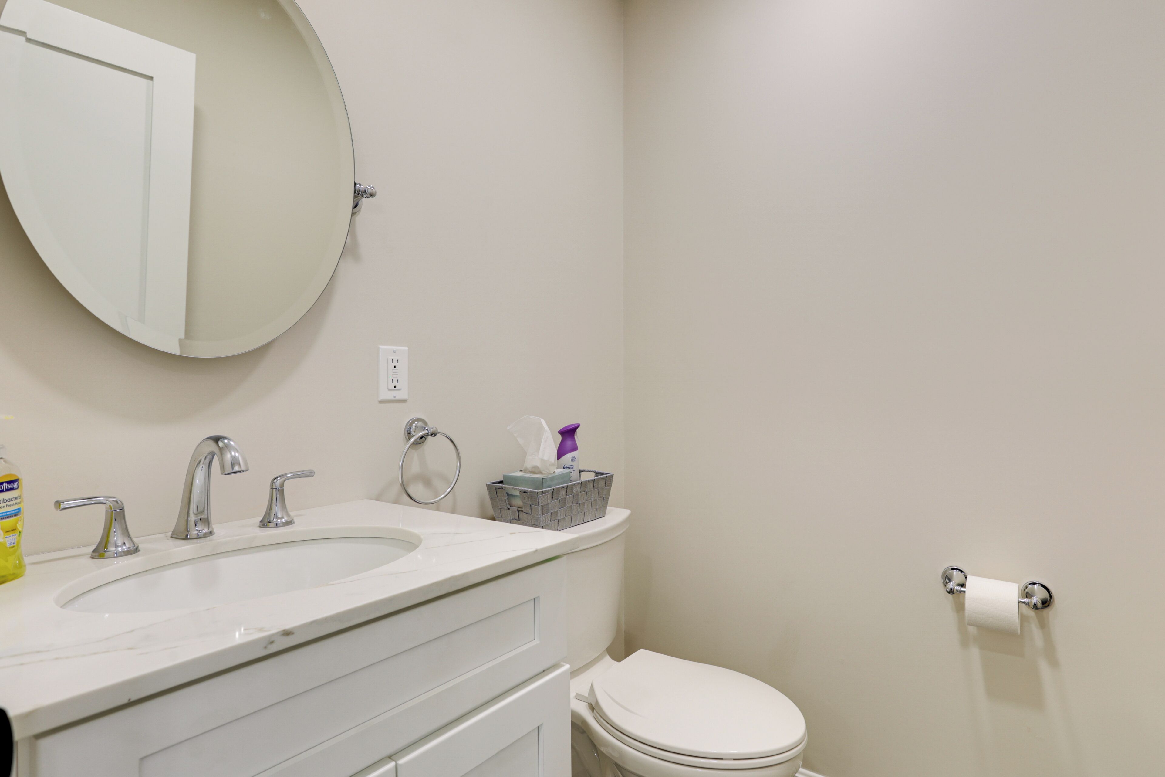 Une salle de bain avec un lavabo blanc, deux robinets, un miroir, des toilettes et un porte-serviettes en papier.