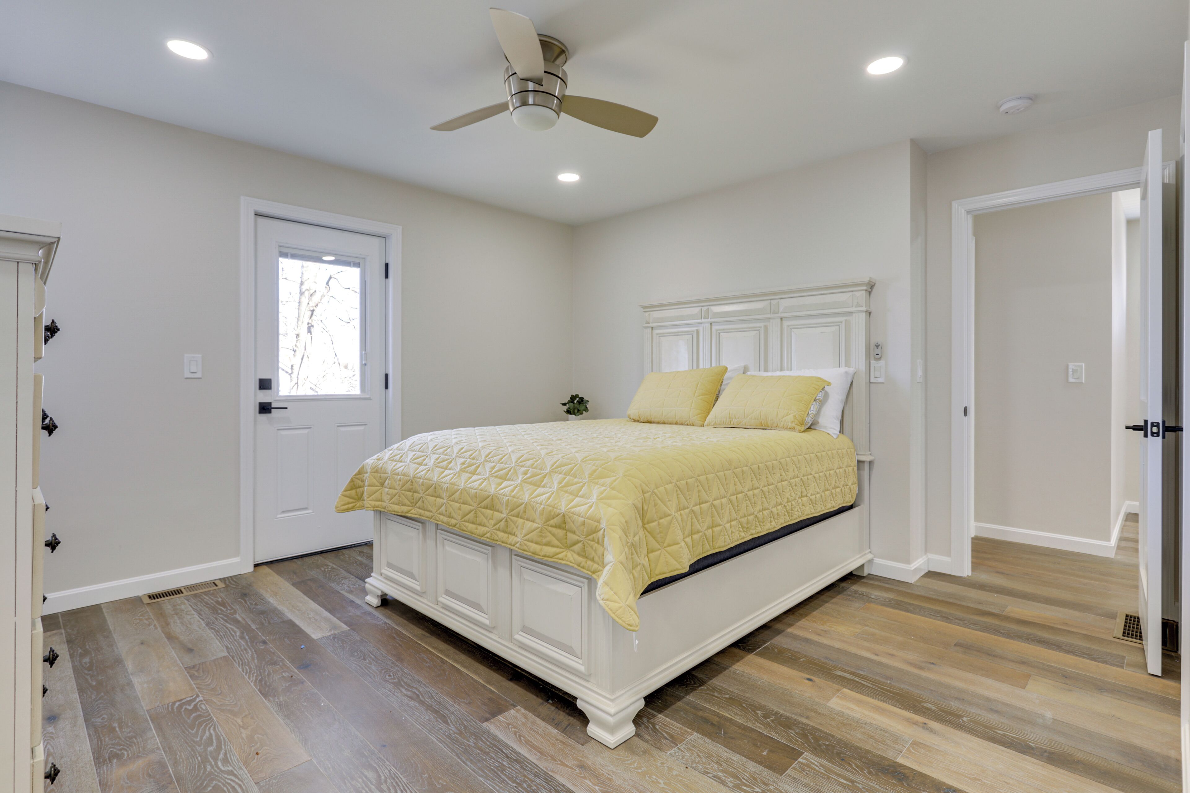 Un dormitorio con cama, ventilador de techo y una puerta con ventanal.