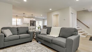 A modern living room with two grey sofas, a patterned rug, and a kitchen in the background. - Renovated Family Home on Providence River! (Riverside)