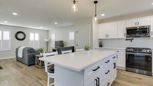 A modern kitchen with white cabinetry, a large island, stainless steel appliances, and pendant lighting. - Renovated Family Home on Providence River! (Riverside)