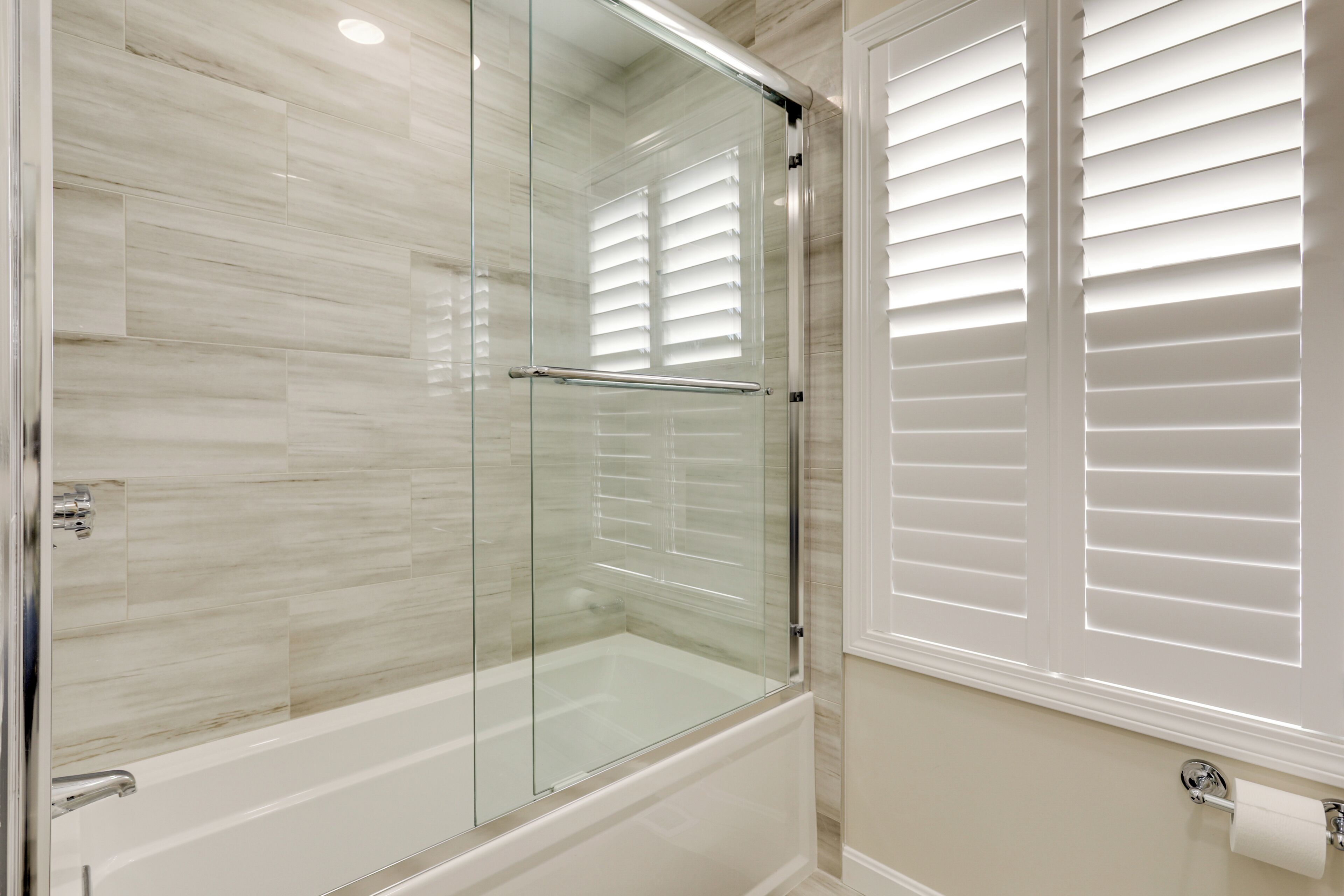 Une salle de bain moderne avec une douche à parois de verre, une baignoire blanche et des toilettes dotées d’un porte-serviettes en papier.