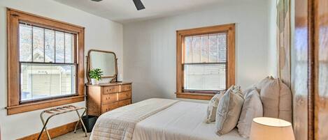 Un dormitorio con cama, cómoda, espejo y dos ventanas con persianas.