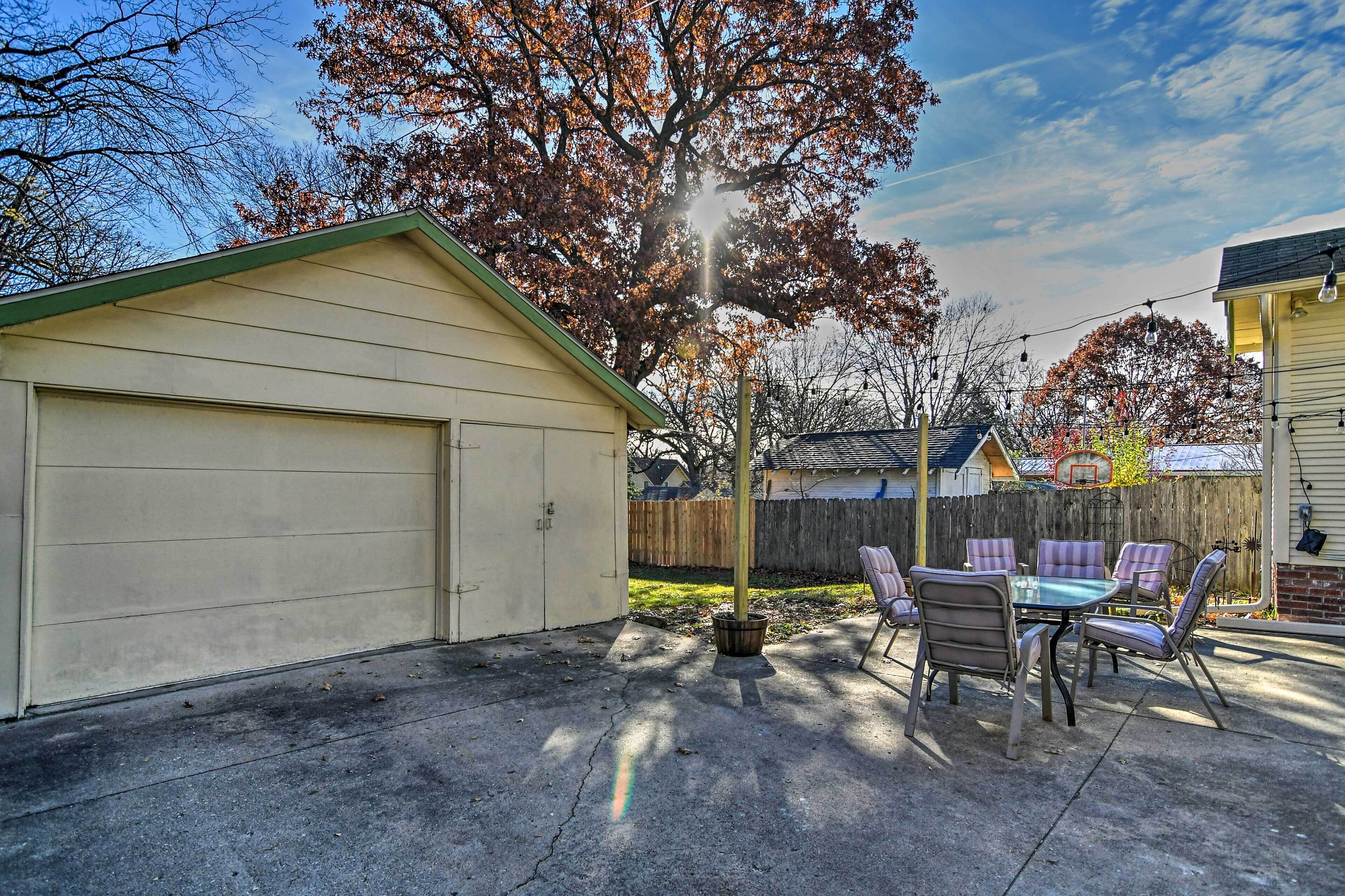 Een garage met een overdekte patio, een houten omheining en een basketbalveld op de achtergrond.
