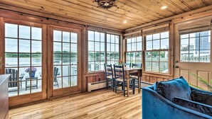 A wooden-paneled room with a dining table and chairs, large windows with a view of a body of water, and a blue sofa. - Charming Bristol Cottage w/ Private Beach! (Bristol)