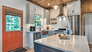 A modern kitchen with white cabinets, a stainless steel refrigerator, a built-in oven, and a marble island. - Charming Bristol Cottage w/ Private Beach! (Bristol)