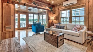 A spacious living room with wooden walls, a white sofa, a blue armchair, and a wooden coffee table. - Charming Bristol Cottage w/ Private Beach! (Bristol)