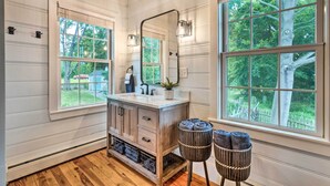 A bathroom with a wooden vanity, a large mirror, and two windows with views of greenery. - Charming Bristol Cottage w/ Private Beach! (Bristol)