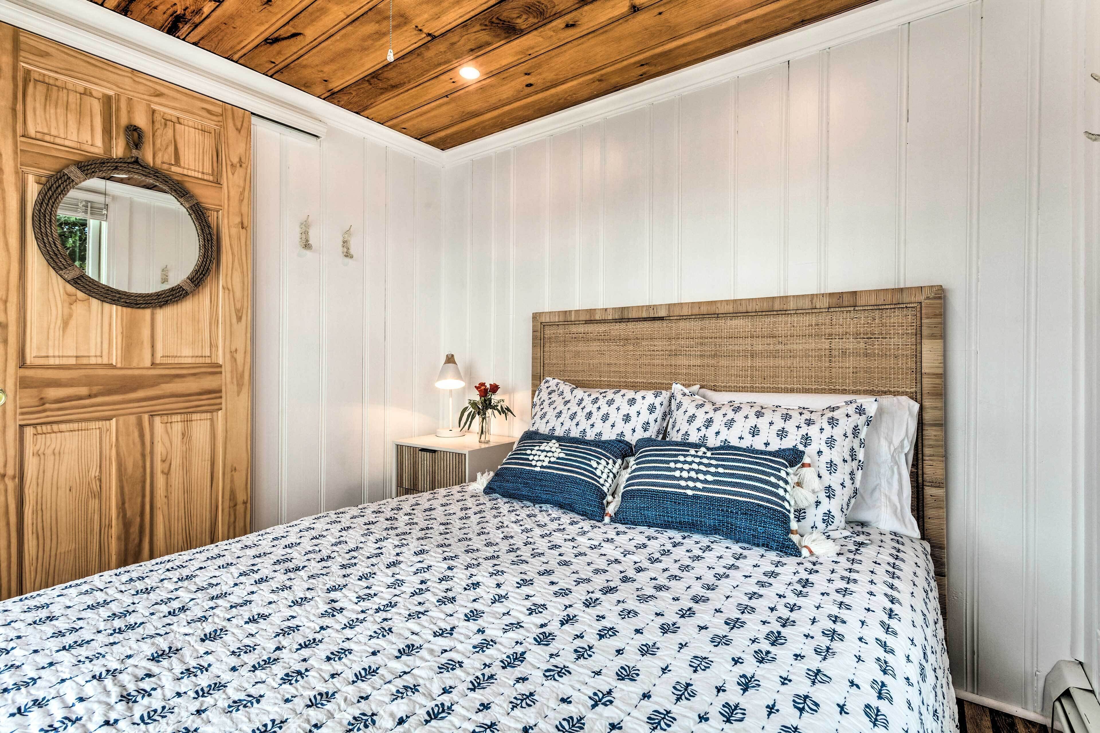 Une chambre avec un plafond en bois, un lit recouvert d’une couvre-lit à motifs, un miroir rond et une table de chevet avec une lampe.