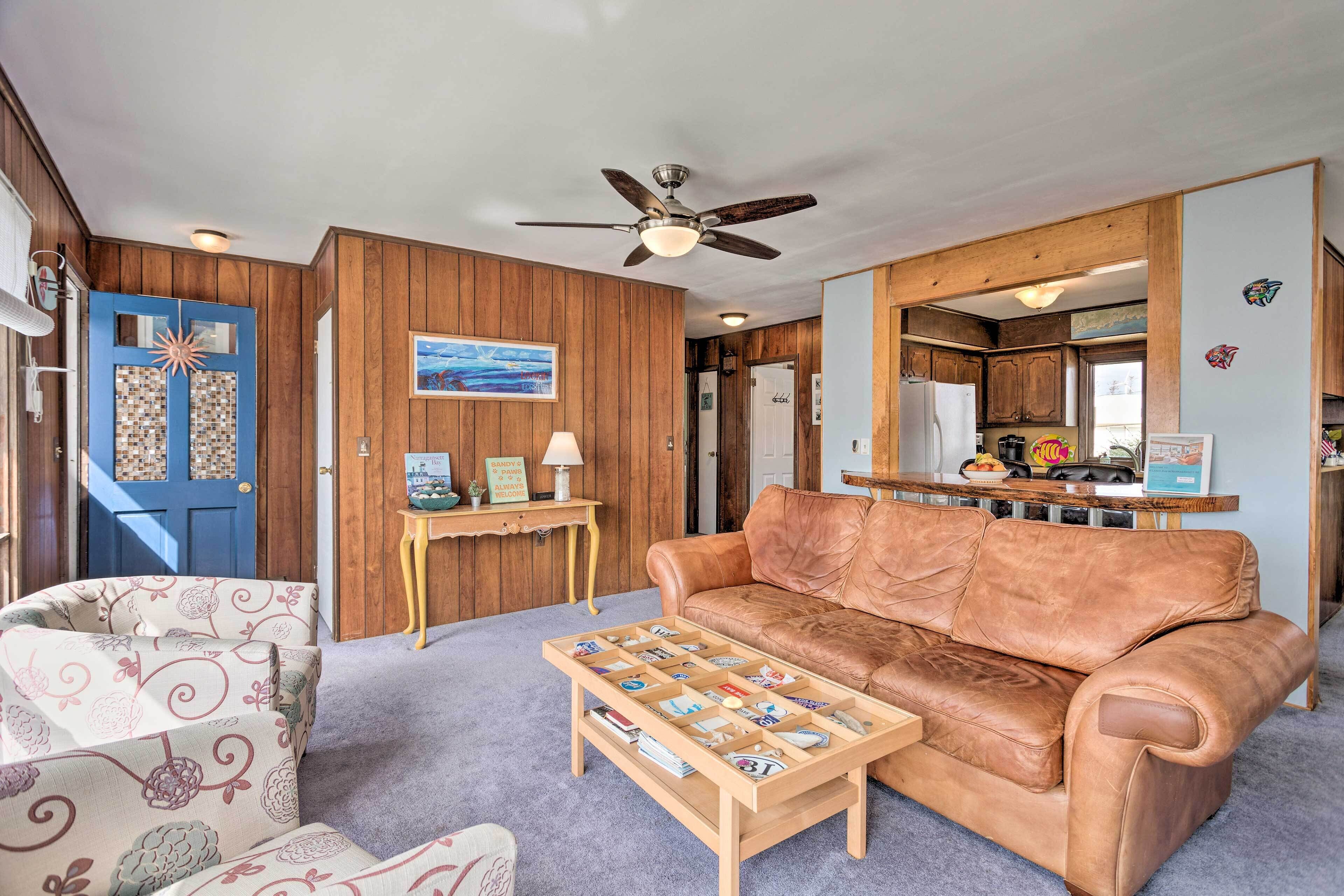 A living room with a brown leather sofa, a patterned armchair, a wooden coffee table, and a ceiling fan.