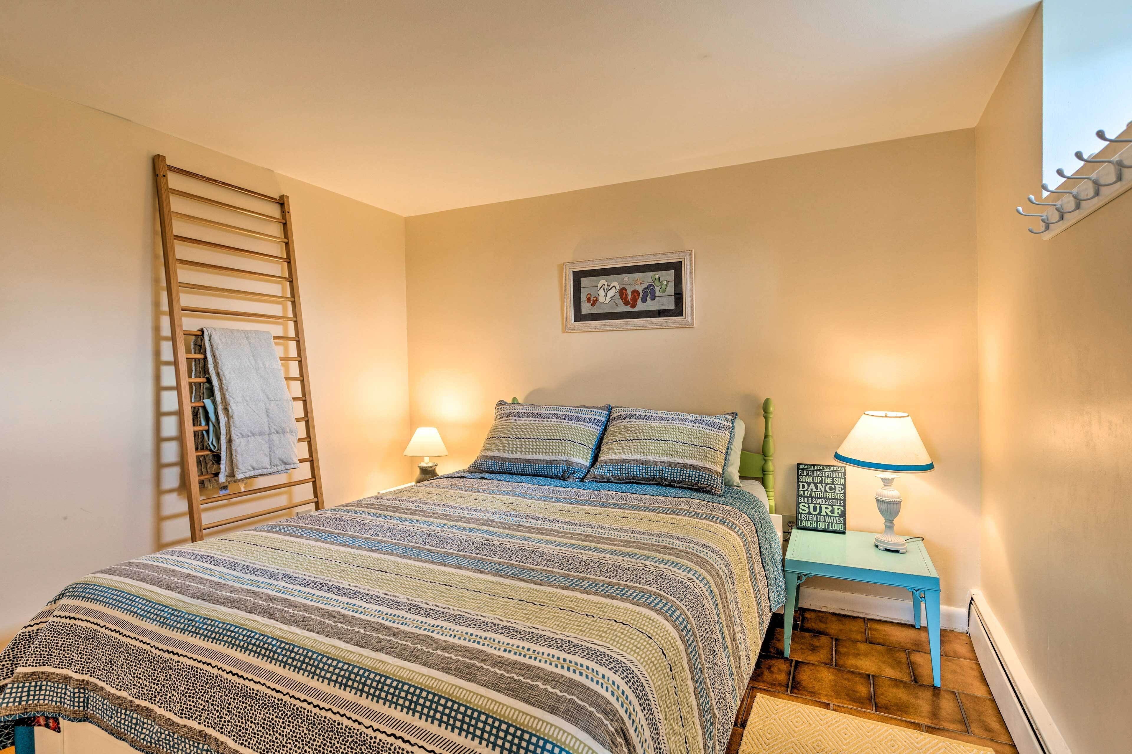 Un dormitorio con una cama, una escalera de madera, un cuadro enmarcado en la pared y una mesita de noche con una lámpara.