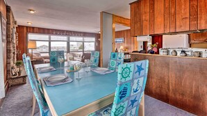 A dining area with a blue table and matching chairs, wooden cabinets, and a view through the window. - Rhode Island Oceanview Retreat: Walk to Shore! (Narragansett)