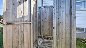 A wooden outdoor structure with a metal door and a small step leading to a gravel area. - Rhode Island Oceanview Retreat: Walk to Shore! (Narragansett)