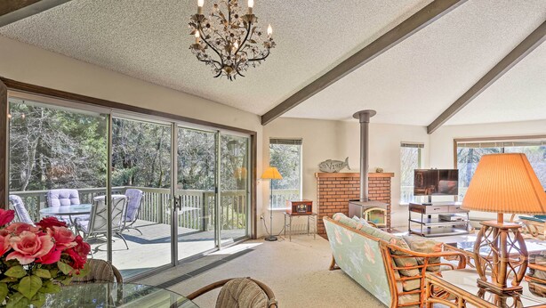 A spacious living room with a glass sliding door leading to a balcony, a fireplace, and a television. - Woodsy Willow Creek Getaway w/ Pool & Deck! (Willow Creek)