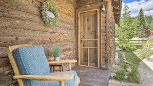 A log cabin with a wooden door, a porch with a chair and table, and a sign above the door. - Walk to Grand Lake: Historic Dtwn Cabin! (Grand Lake)