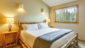 Un dormitorio con una cama grande, dos mesitas de noche con lámparas y una ventana con vista a árboles.