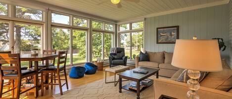 A spacious living room with a dining area, large windows, a ceiling fan, and a cozy seating arrangement.