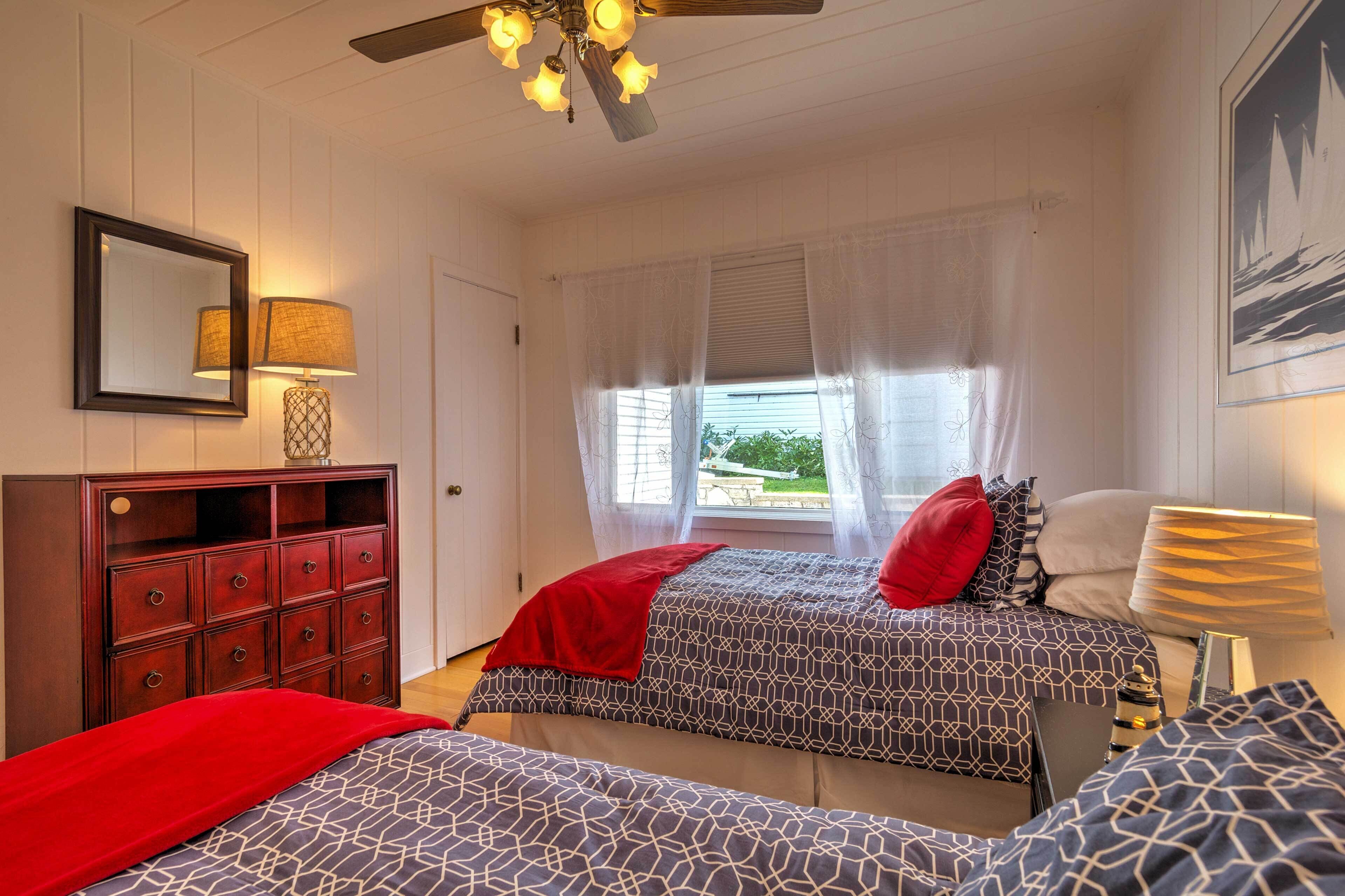 A bedroom with two beds, a dresser, a ceiling fan, and a window with curtains.