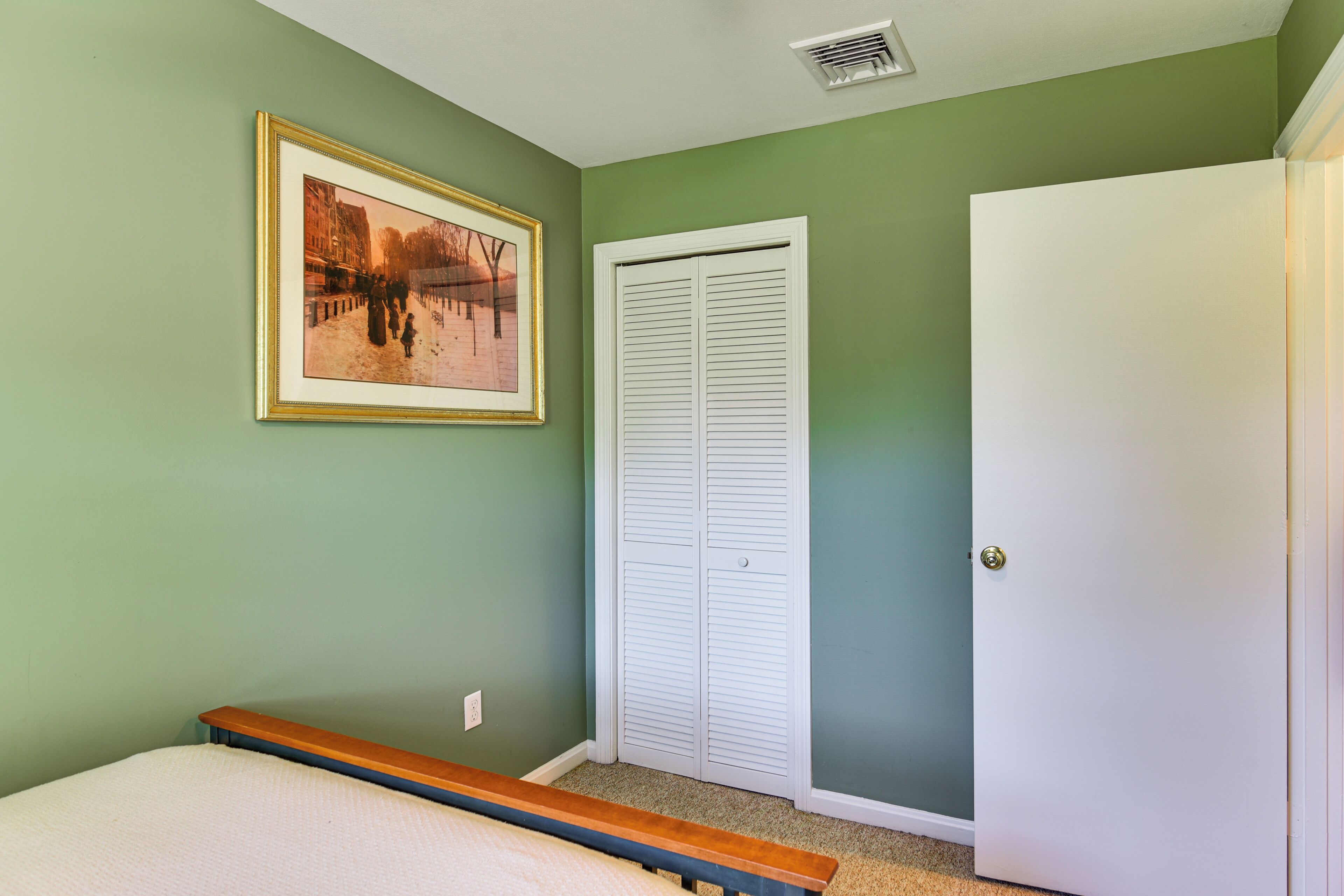 A bedroom with a bed, a framed picture on the wall, a white closet, and a door.