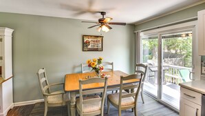 A dining area with a wooden table and chairs, a ceiling fan, and a view of the outdoors through large windows. - Bright Narragansett Beach Escape w/ Deck & Yard! (Narragansett)