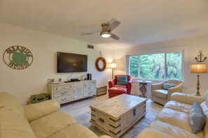 A living room with a ceiling fan, a television, a fireplace, and a large window with a view of trees. - Siesta Key Condo w/ Heated Pool < 1 Mi to Beach (Siesta Key)